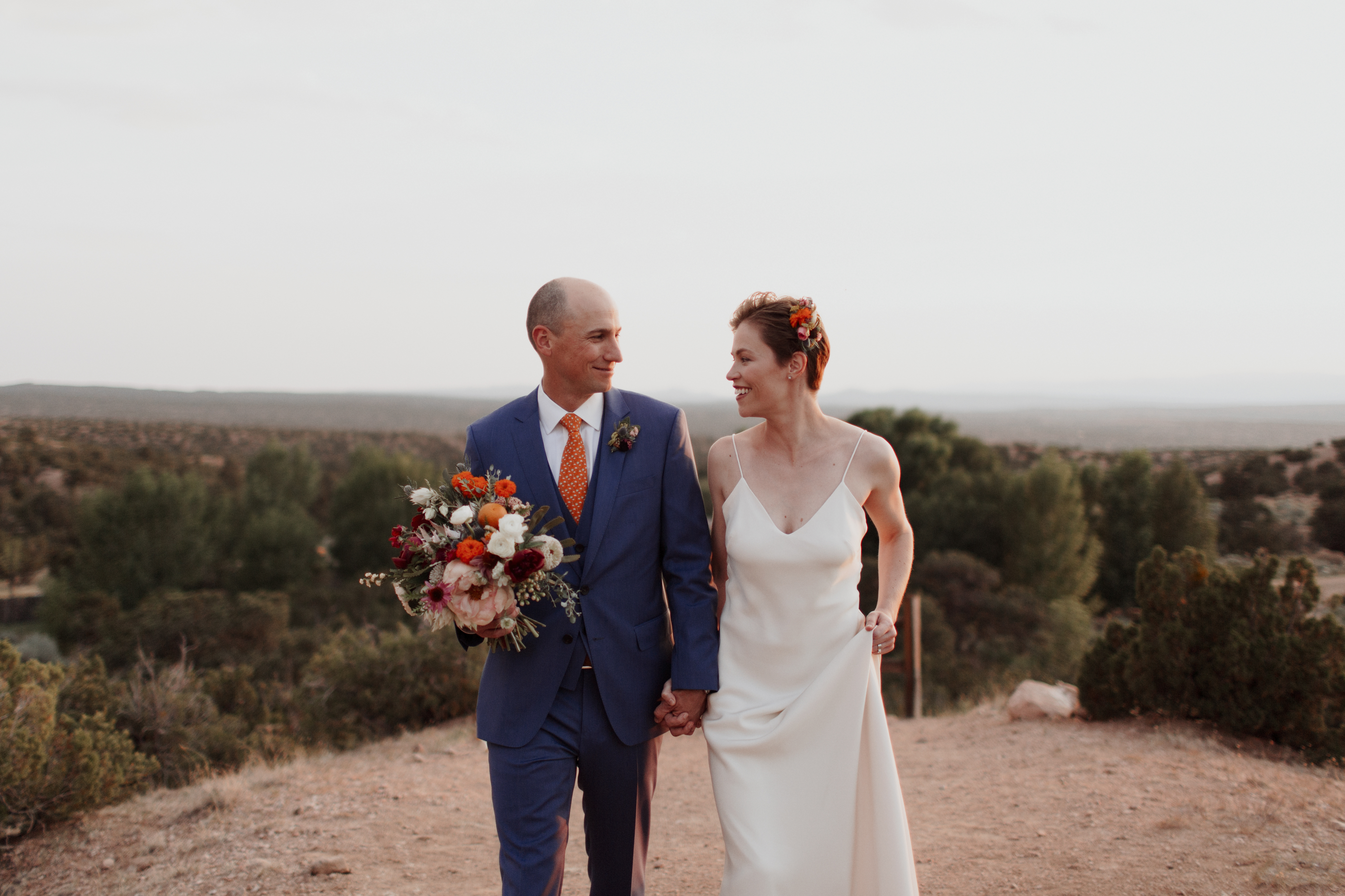 landscape romantic simple updo flowers jewel tones wedding outdoor ceremony planning New Mexico design inspiration orange blue suit silk gown bouquet vows officiants real hair bridal photography romantic couple natural light