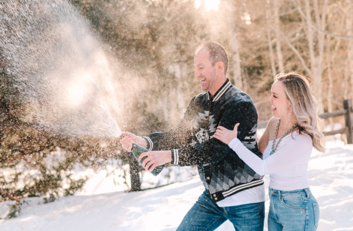 Newly engaged Colorado couple celebrates by opening a bottle of champagne in the snow.